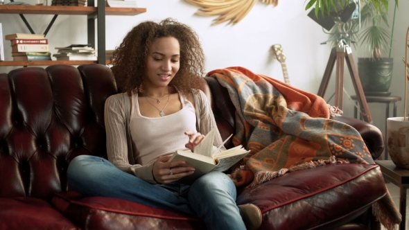 Young Happy Latin Woman Read Paper Book for Education Sitting Alone on Comfort Leather Sofa