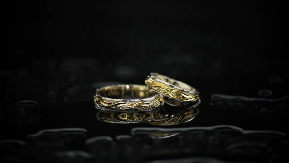 Gold Rings On Black Wet Surface On Black Background