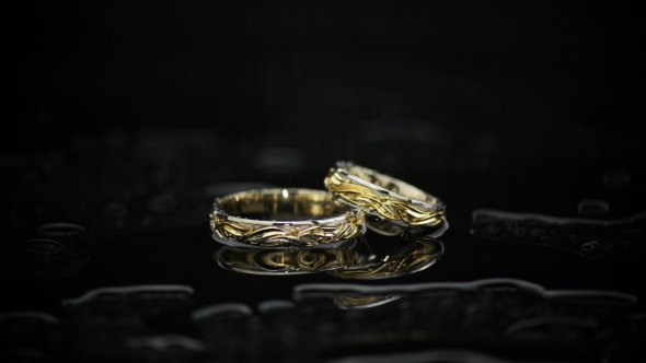 Gold Rings On Black Wet Surface On Black Background alt