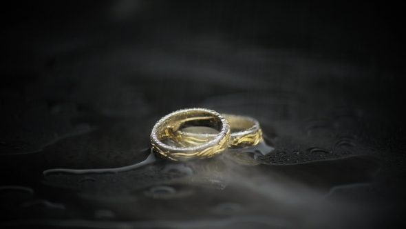Gold Rings On Black Wet Surface On Black Background In Smoke