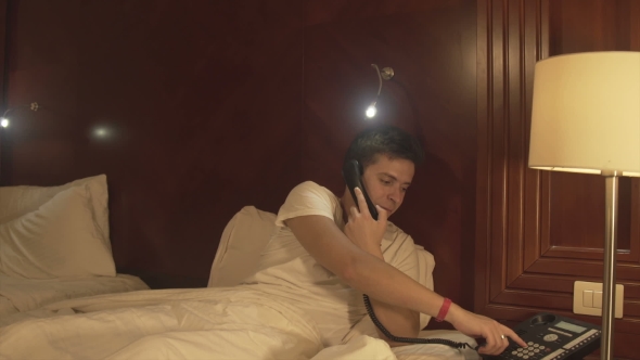 A Young Man Talking on the Phone in the Hotel Bed alt