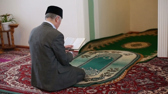 An Old Mullah Praying with the Koran in His Hands alt