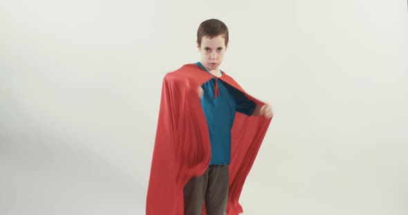 Boy with a superhero cape pretends to fly on a white studio background alt