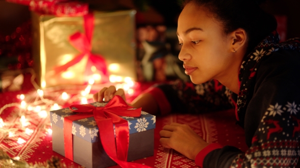 Young Black Woman Is Openning a Gift Box with Red Ribbon on Christmas Night alt