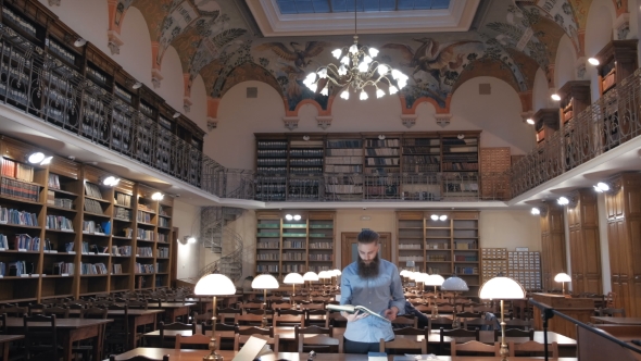 Portrait of a Pensive Bearded Man Student in Sitting at the Library Desk alt