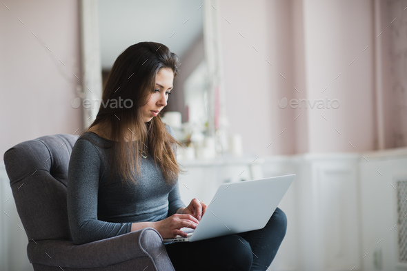 Young woman in modern luxury apartment, sitting comfortable in armchair holding computer on her laps - Stock Photo - Images