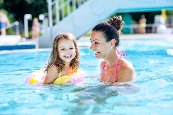 Mother and daughter in swimming pool, aquapark. Sunny summer.