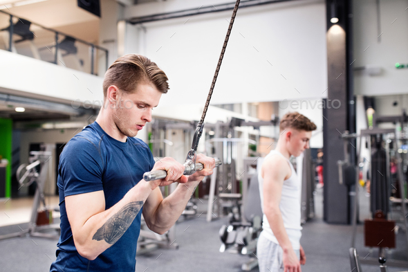 Fit young man in gym working out on pull-down machine.