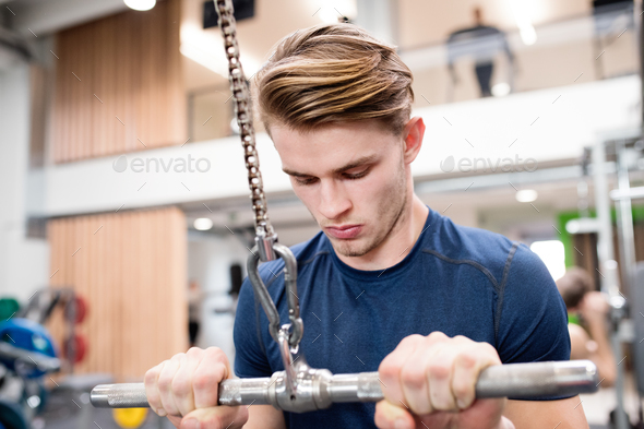 Fit young man in gym working out on pull-down machine.