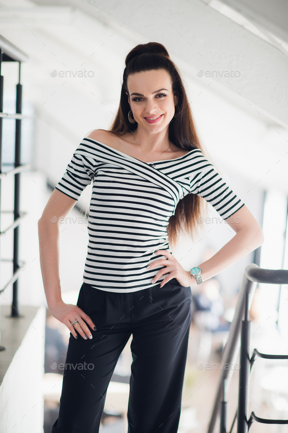 Image of young happy woman dressed in blouse standing in cafe while looking at camera. Stock Photo by romankosolapov