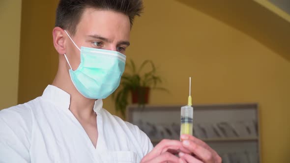 Young Doctor in Protective Mask Preparing Syringe for Injection. Close Up of Young Intern in alt