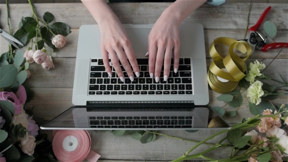 A Woman Is Working By Using a Laptop Computer on Table. Hands Typing on a Keyboard. Flower Shop alt