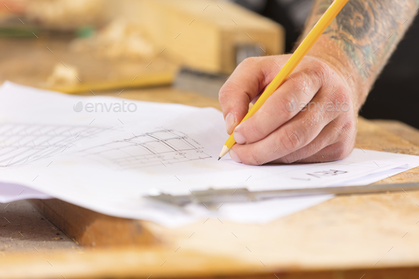 Close-up of carpenter plans project and writes at drawings in workshop - Stock Photo - Images