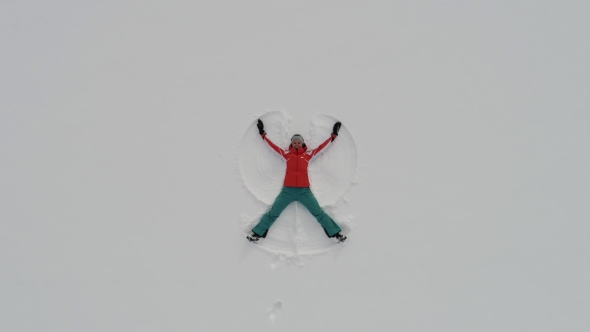 Woman Making Snow Angel Lying in Pure White Snow