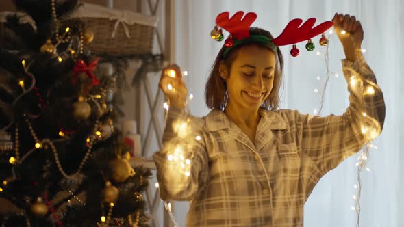Portrait of Happy Cheerful Pretty Woman Wearing Pajama and Reindeer Antlers Headband Dancing with alt
