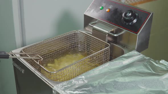 Culinary Worker Is Lowering Sliced Potatoes Inside Boiling Oil in Electric Fryer alt