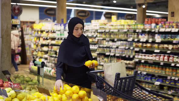 Muslim Woman Shopping for Groceries Taking Lemons From the Fruit Aisle alt