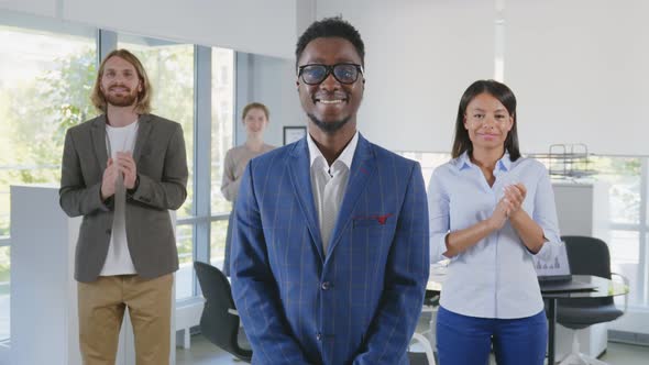 African Young Boss Smiling at Camera with Diverse Team Applauding on Background alt