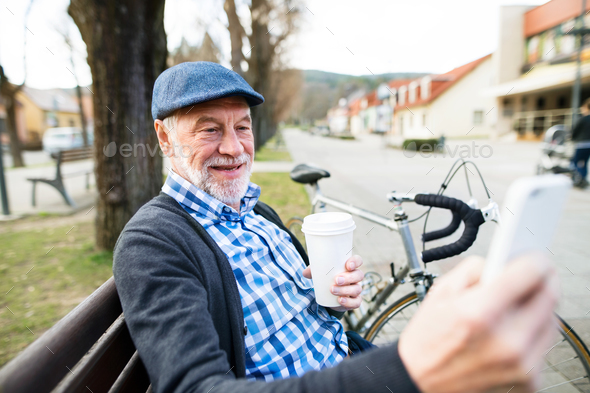 Senior man with bicycle in town, taking selfie with smart phone