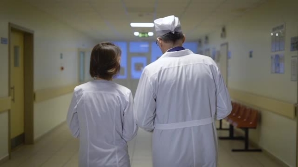 Download Back View Of Male And Female Doctors Dressed In Lab Coats Walking Through The Corridor Of The Ward By Pampampam