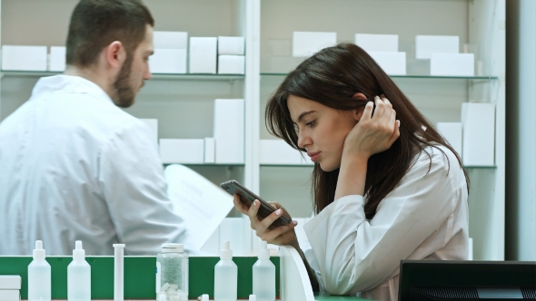 Bored Female Pharmacist Use Mobile Phone at Pharmacy alt