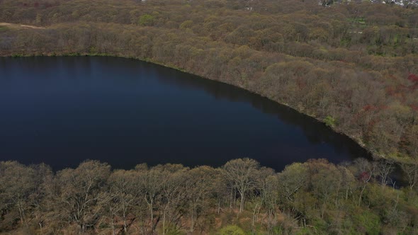 An aerial view of a dark lake during a sunny day. The drone camera dolly in & tilt down then pan lef alt