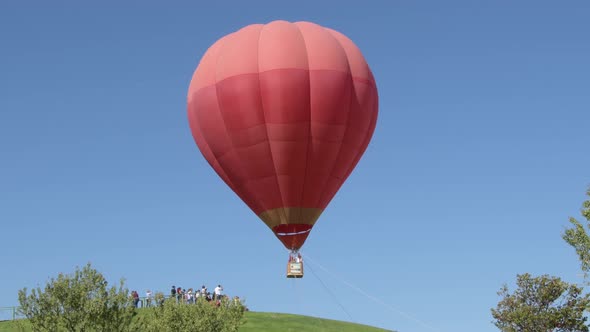 Red Hot Air Balloon Taking Off with Travelers in Their Basket alt