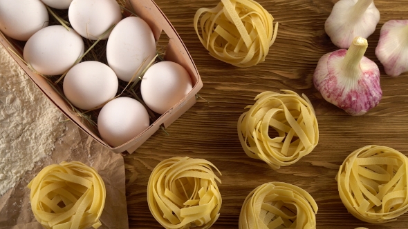 Pasta, Eggs, Oil, Tomatos, Garlic and Flour on Wooden Background