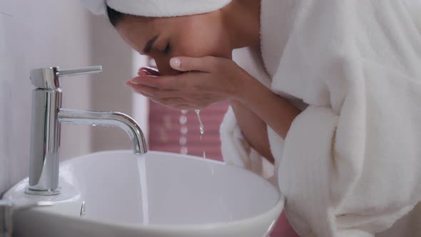 Closeup Young Happy Woman with Towel on Head in White Bathrobe Washes Face in Bathroom Refreshes alt
