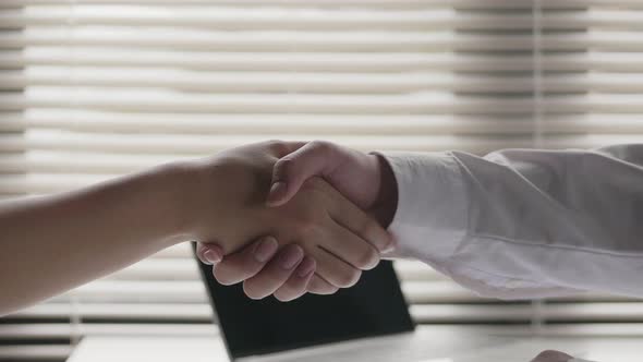 Asian businessman shaking hands with businesswoman partners while sitting at the office.