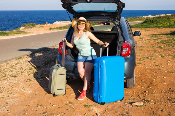Travel, summer holidays and vacation concept - Young woman with suitcases on car trip.