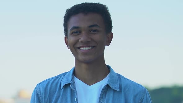 Happy African-American teenager boy smiling at camera outdoors alt