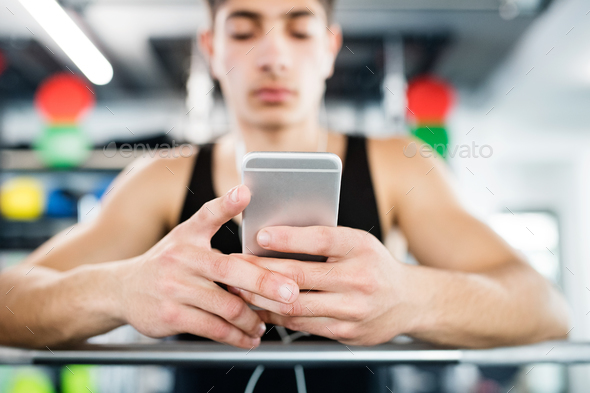 Hispanic man in gym resting, holding smart phone,listening music