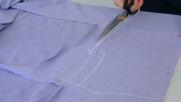 Hands of Seamstress Cutting Fabric with Scissors