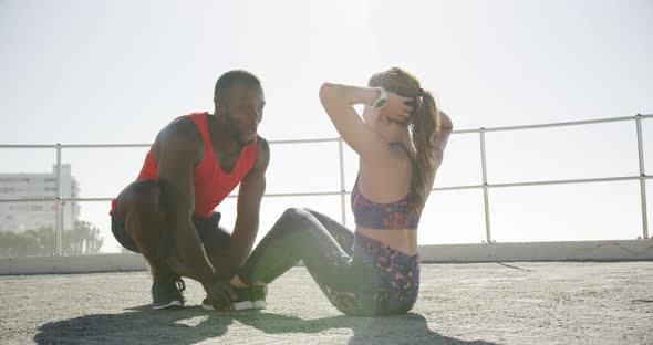 Man helping woman to perform abdominal exercise on a promenade 4k
