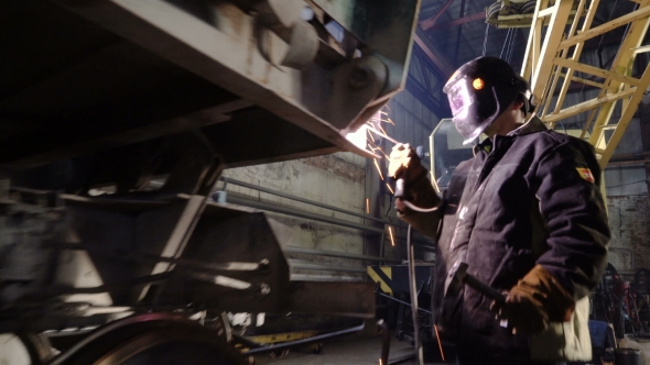 Tracking Shot of Welder in the Protactive Mask Starting To Weld the Metal Parts of the Broken