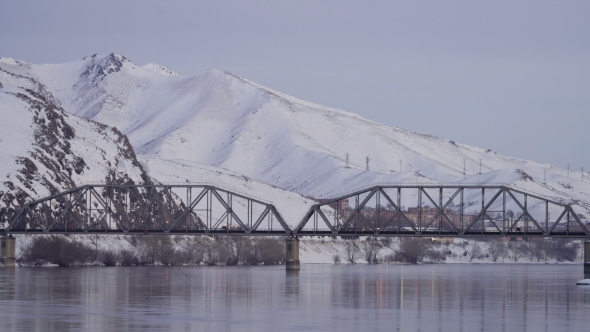 Traffic on Highway in the Background of Railway Bridge Over the River By Snowy Mountains