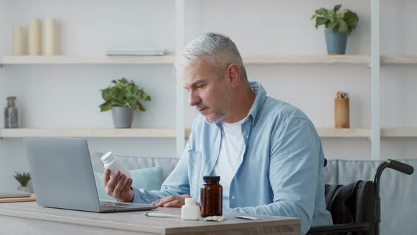 Disabled Senior Man Holding Medication Bottle Browsing Internet At Home alt