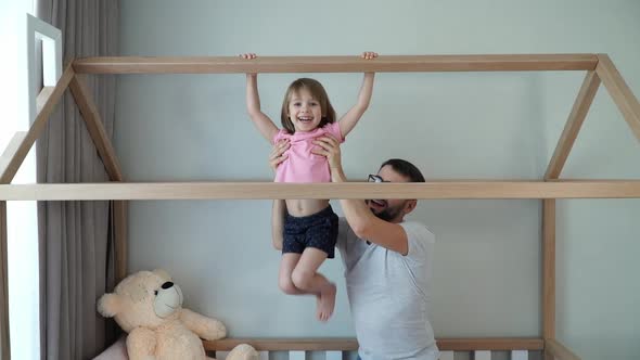 Father Helps Girl Pull Up on Horizontal Bar on Crib at Home