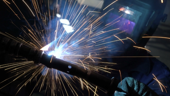 Welder Builds Up the Metal on the Workpiece. Sparks From Welding. Welding Mask