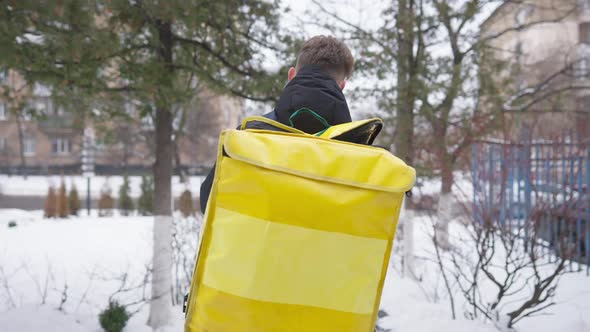 Back View of Young Man Hanging Food Delivery Backpack and Walking Away on Winter Day Outdoors alt
