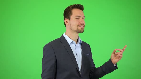 A Young Handsome Businessman Smiles and Points at Objects Floating Around Him - Green Screen Studio alt