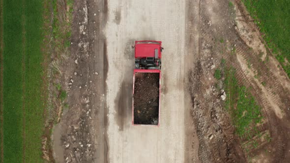 Red Lorry Carrying Soil From the Field Along a Dirt Road Between Two Green Fields alt