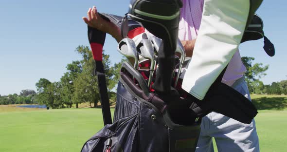 Caucasian senior man walking with his golf bag at golf course on a bright sunny day alt