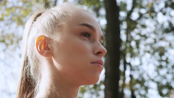 Young Pretty Female with Ponytail Looks Around Outdoors at Sunny Autumn Park