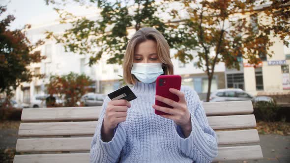 Woman wearing medical mask using smartphone and credit card for online shopping. Banking. alt