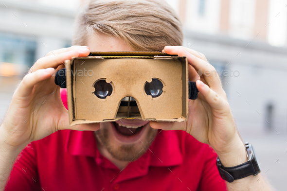 Close-up of funny man using cardboard virtual reality goggle outdoors