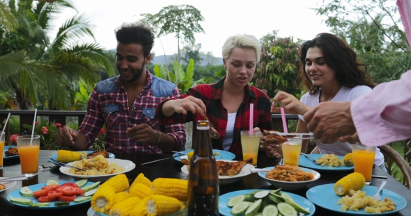 Man Passing Food To People Sitting At Table Eating Young Friends Group Gathering On Summer Terrace