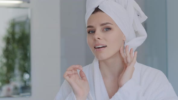 Attractive Millennial brunette woman in bathrobe looking at herself at camera in the mirror alt