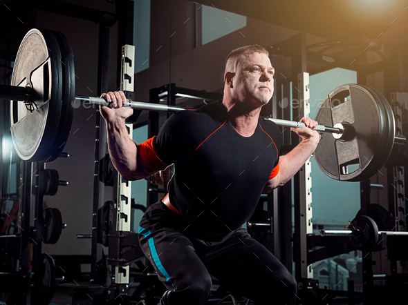 Portrait of super fit muscular young man working out in gym with barbell - Stock Photo - Images